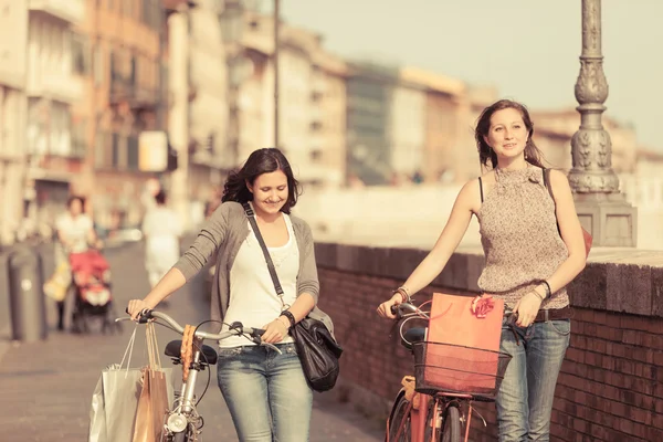 Duas mulheres bonitas andando na cidade com bicicletas e sacos — Fotografia de Stock