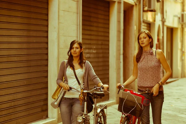 Две красивые женщины, гуляющие по городу с велосипедами и сумками — стоковое фото