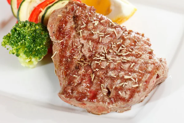 Biftek se zeleninou na bílé desce — Stock fotografie