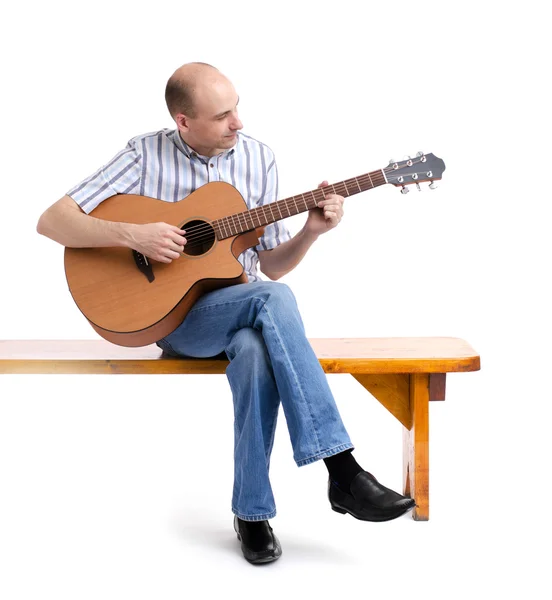 Pohledný mladý muž hrát na kytaru, sedí na lavičce — Stock fotografie