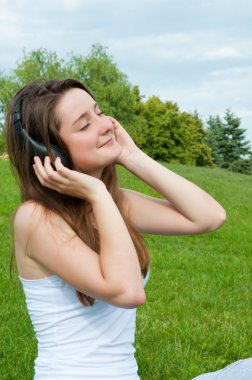 Girl in headphones listens to music in the park. clipart