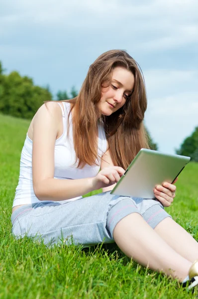 Flicka med tabletten i parken på gräs. — Stockfoto