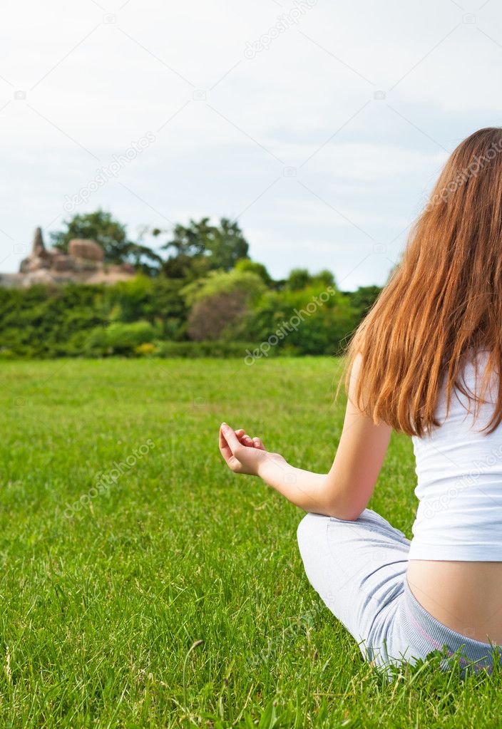Girl meditates on lawn in garden.
