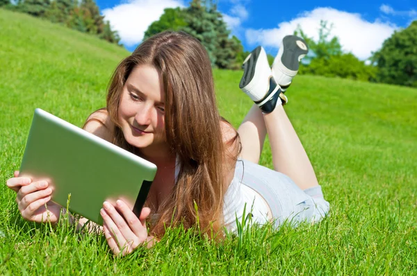 Mooie jonge vrouw met Tablet PC liggend op gras. — Stockfoto