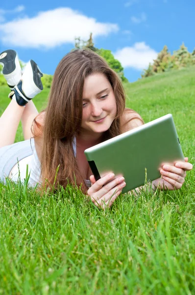 Lachende gelukkig meisje liggend op gras met Tablet PC. — Stockfoto