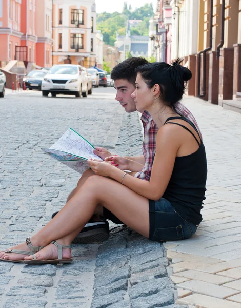 Menina e um cara sentado na beira da estrada com um mapa . — Fotografia de Stock