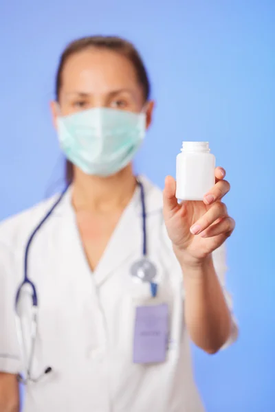 Médico (mulher) segurando recipiente com remédio no backgroun azul — Fotografia de Stock