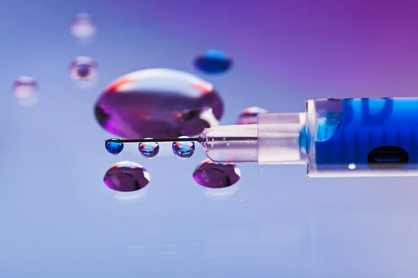 Sprutans nål med vätska som droppar på droppar vatten bakgrund, ma — Stockfoto