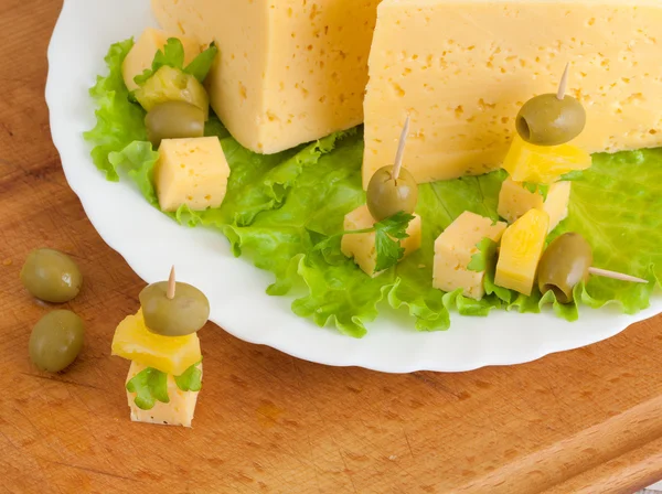 Sýr se zelení a olivami na dřevěné desce — Stock fotografie