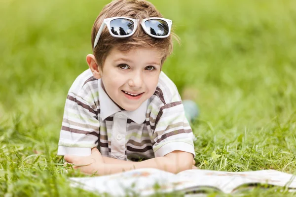 Beleza sorridente criança menino leitura livro ao ar livre — Fotografia de Stock