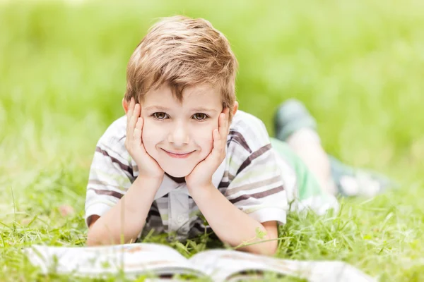 Красивый улыбчивый мальчик, читающий книгу под открытым небом — стоковое фото
