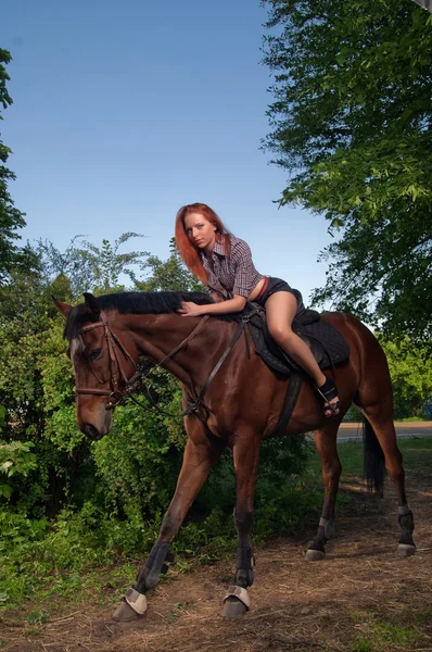 Kvinna med rött hår som sitter på en häst — Stockfoto