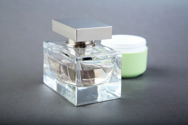 Пляшка парфумів і трубки косметичного крему на сірому — стокове фото