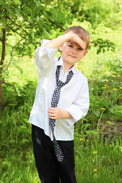 Der kleine Junge bindet eine Krawatte gegen Grün — Stockfoto