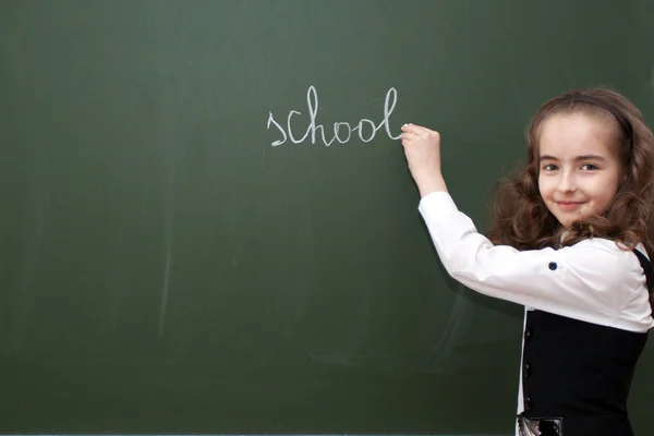 Schoolgirl writes on a blackboard — Stock Photo, Image
