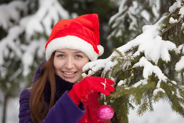 Frau mit Weihnachtsmütze schmückt Fichte — Stockfoto