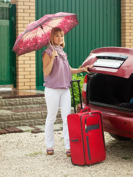 Девушка кладет чемодан в машину — стоковое фото
