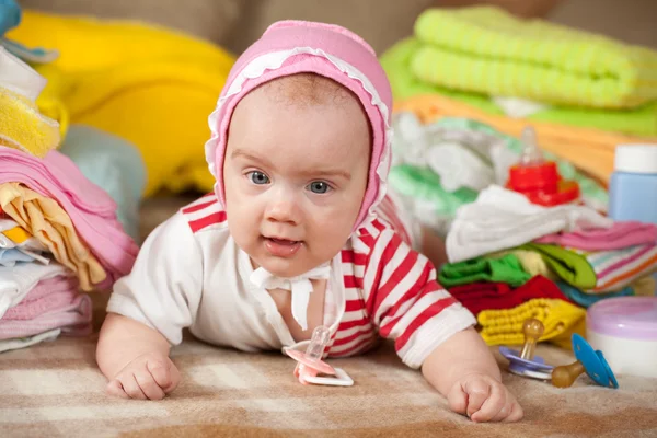 Baby girl with heap of baby's wear — Stock Photo, Image