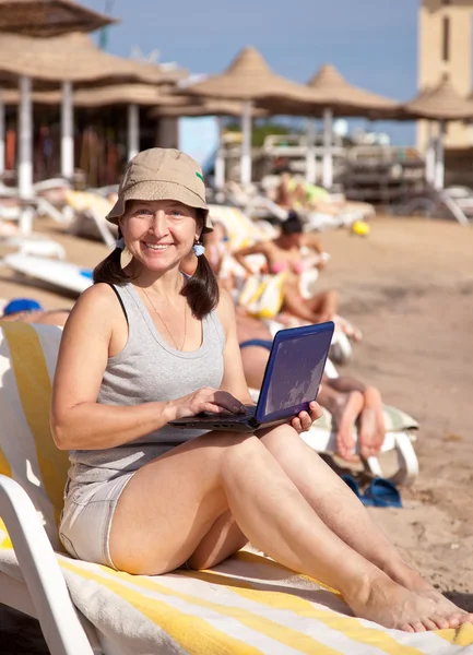 Mutlu bir kadın laptop ile kumsalda oturuyor — Stok fotoğraf