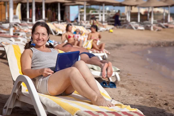 Modent kvinne med bærbar PC på stranden – stockfoto