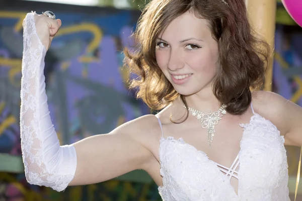 The girl in a white dress shows muscles on a hand — Stock Photo, Image