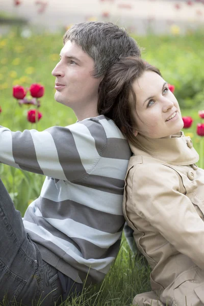 O homem e a mulher estão sentados contra uma cama com tulipas. — Fotografia de Stock