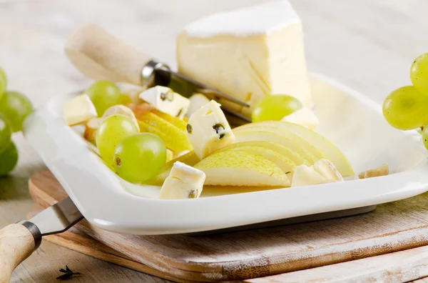 Cheese and grapes on wooden platter — Stock Photo, Image