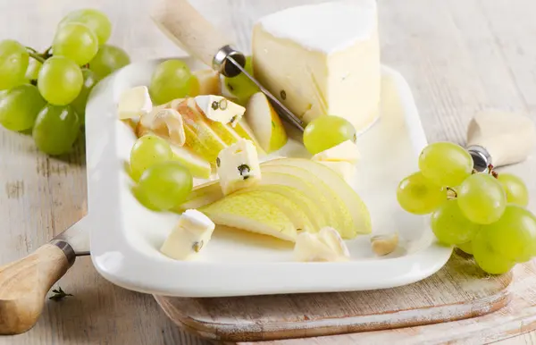 Cheese and grapes on wooden platter — Stock Photo, Image