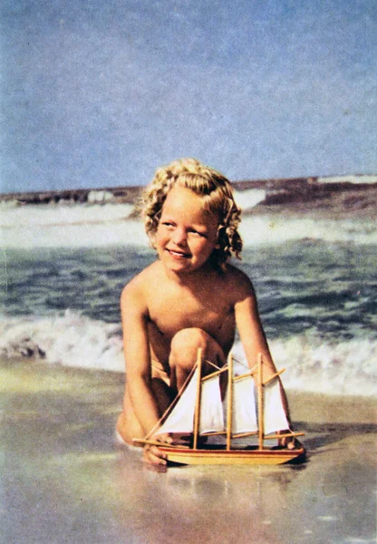 Flicka med en modell segelbåt på stranden — Stockfoto