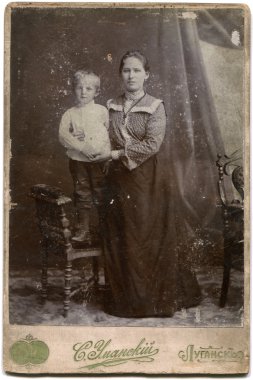 RUSSIA - CIRCA the end of 19 - early 20 century: An antique photo shows woman with a boy on a chair, Lugansk, Russian Empire Russian text: Umanskiy (photographer), Lugansk clipart