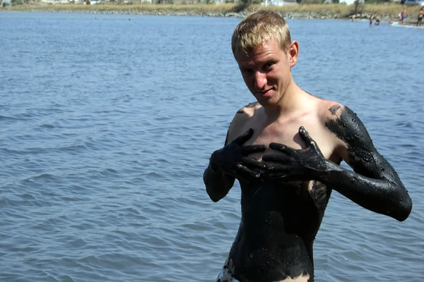 Nuori mies mudan peitossa suolaisessa järvessä — kuvapankkivalokuva