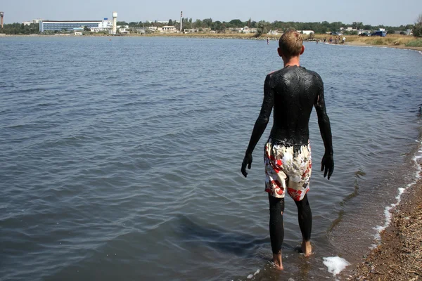 Nuori mies mudan peitossa suolaisessa järvessä — kuvapankkivalokuva