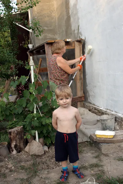 Маленький мальчик позирует на фоне женщины рисует дом — стоковое фото