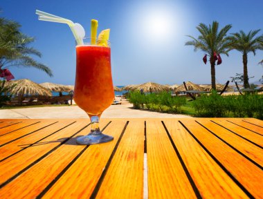 Glass of tasty juice with pipe on the table next to beach. Egypt clipart