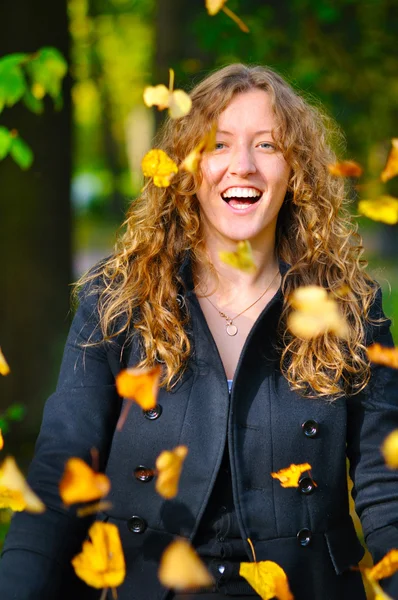 Glückliche Frau wirft trockenes Herbstlaub in Park — Stockfoto