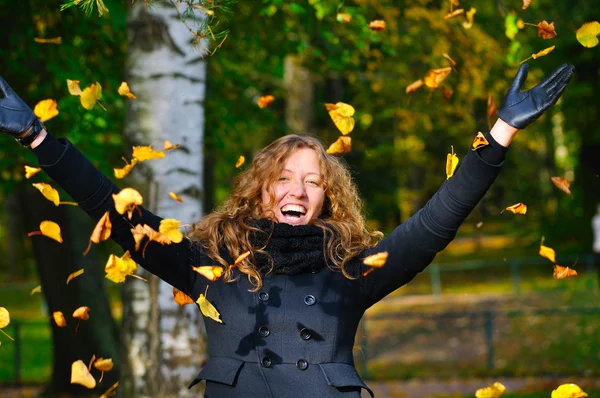 Ευτυχισμένη γυναίκα ρίχνει ξηρά φύλλα φθινόπωρο στο πάρκο — Φωτογραφία Αρχείου