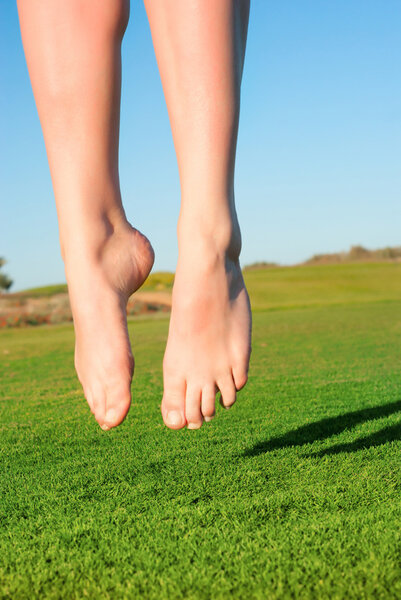 Closeup of feet of jumping on green field woman