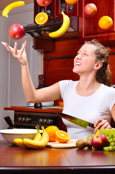 Happy woman is cooking fruit salad out of flying fruits — Stock Photo, Image