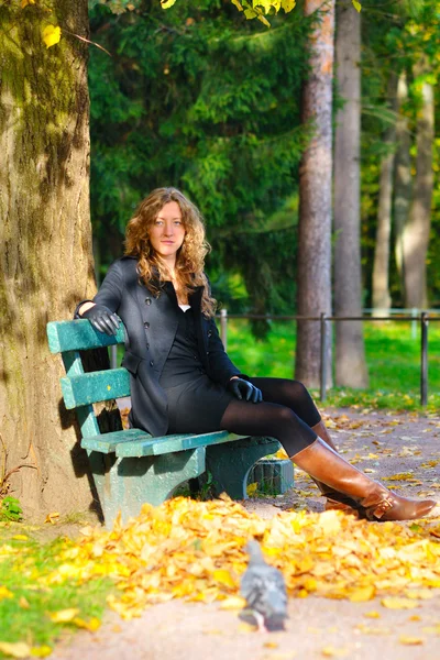 Mladá žena sedí na lavičce v podzimním parku a při pohledu — Stock fotografie