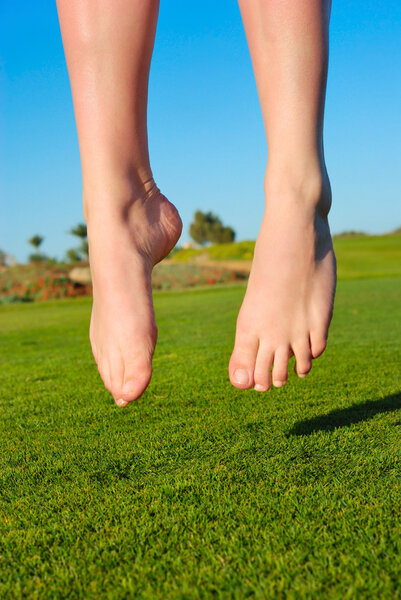 Closeup of feet of jumping on green field woman