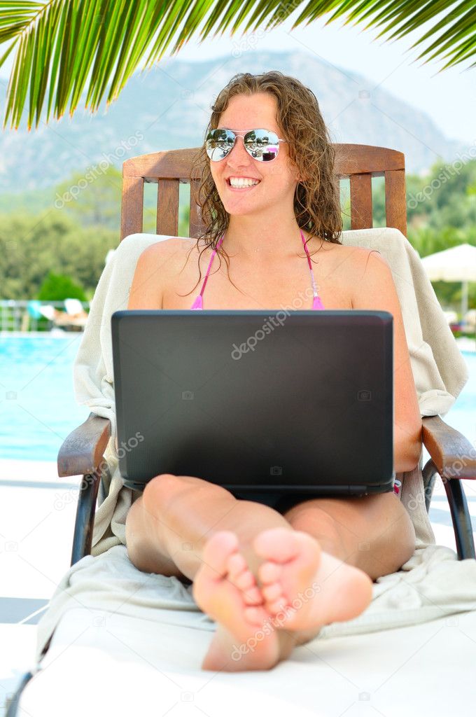 Beautiful woman is sitting on wooden chair near thr pool with la