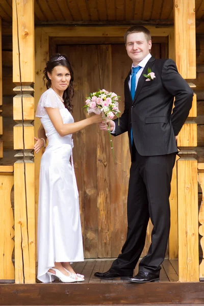 Braut und Bräutigam mit einem Strauß auf einer Holzveranda — Stockfoto