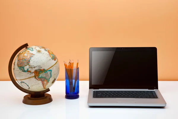Students desk with globe, pens and laptop — Stock Photo, Image