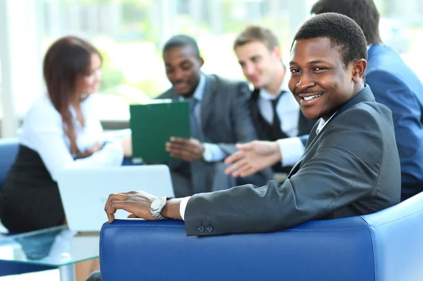 Портрет улыбающегося афроамериканского бизнесмена с руководителями, работающими на заднем плане — стоковое фото