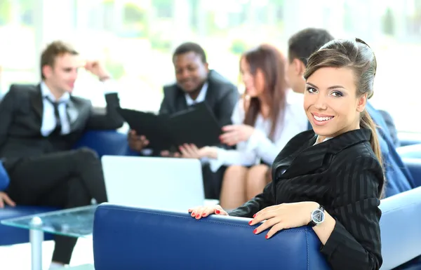 Nahaufnahme einer hübschen jungen Geschäftsfrau, die bei einem Treffen mit ihren Kollegen im Hintergrund lächelt — Stockfoto