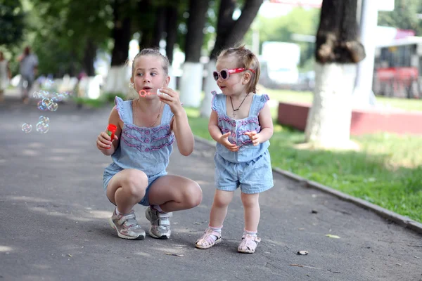 Dwie siostry na ulicy gra z baniek mydlanych — Zdjęcie stockowe