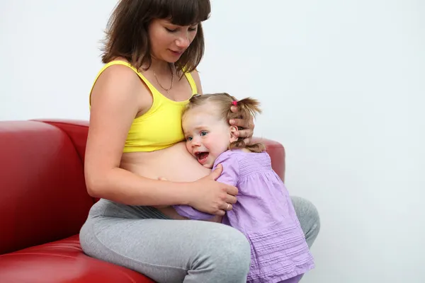 Ung flicka lyssna på hennes gravid mamma mage — Stockfoto