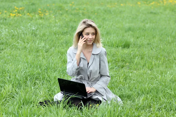 Girl working on laptop and talking on cell phone — Stock Photo, Image