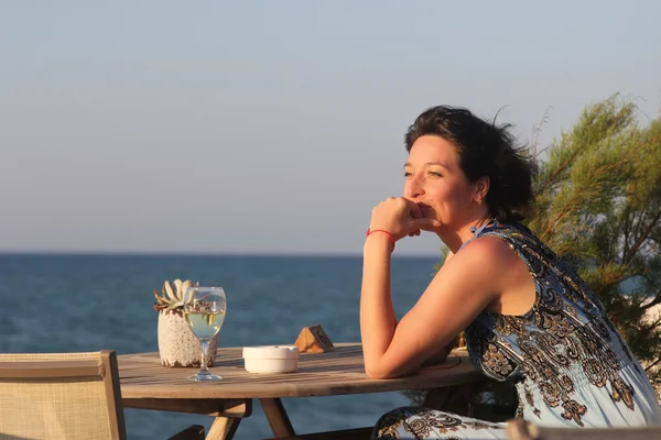 女人坐在户外咖啡馆与海洋 b 上的白色藤 glas — 图库照片