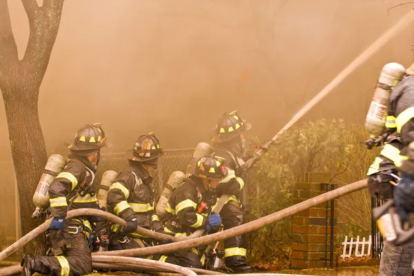 Bomberos en el trabajo apagando un incendio en la casa —  Fotos de Stock